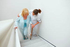 Female nurse assisting elderly patient to climb stairs